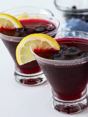 Two blueberry martini cocktails in stemless martini glasses.